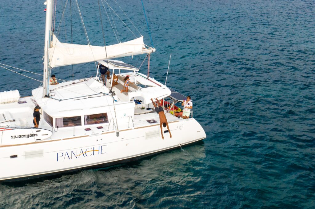 A vibrant scene of people snorkeling in clear blue waters, with a catamaran anchored nearby amidst a picturesque coastal landscape.