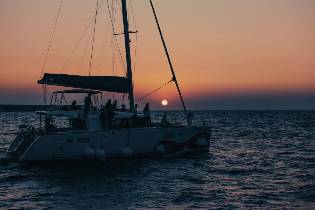 A sailboat silhouetted against a vibrant sunset sky, with people enjoying a catamaran tour costa rica on the open water.

