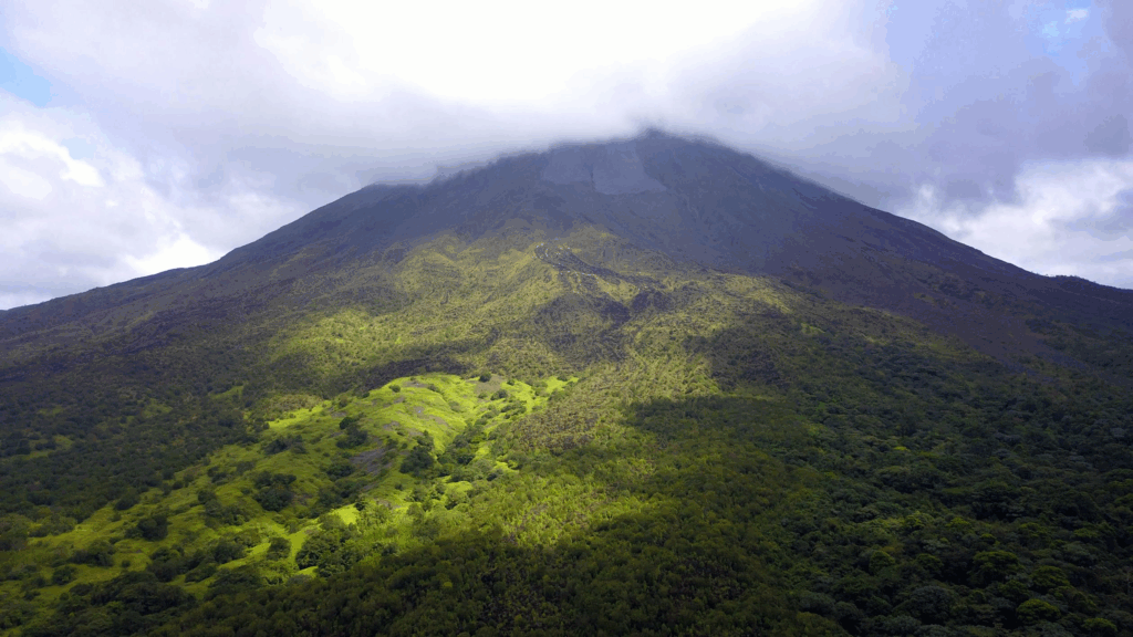 Aerial view of a lush green mountain with a partially cloudy summit and surrounding vegetation