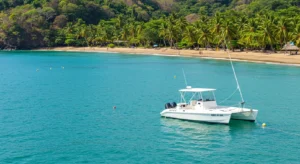 White catamaran near palm-lined beach showing is Costa Rica safe travel.